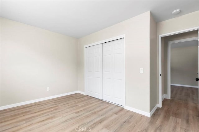 unfurnished bedroom with a closet, light wood finished floors, and baseboards