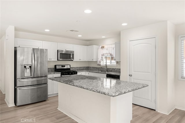 kitchen featuring white cabinetry, a kitchen island, light stone countertops, appliances with stainless steel finishes, and light wood finished floors