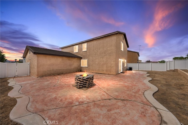 back of house at dusk featuring stucco siding, a patio area, a fenced backyard, and an outdoor fire pit