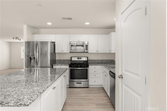 kitchen with light wood-type flooring, stainless steel appliances, white cabinets, light stone countertops, and visible vents