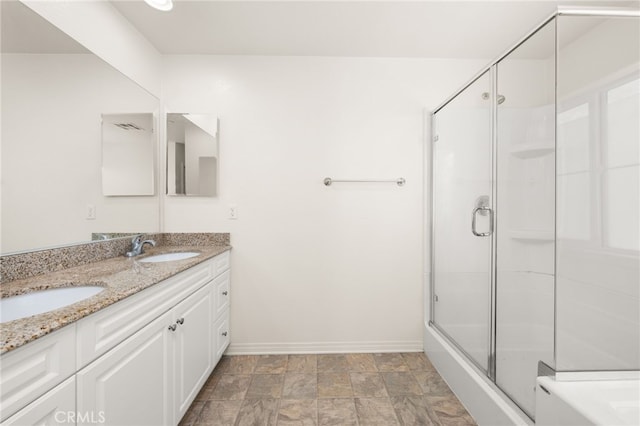 bathroom featuring a shower with shower door, double vanity, baseboards, and a sink