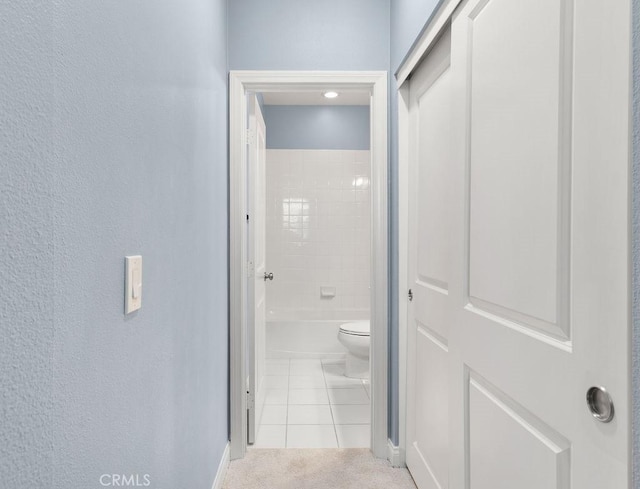 hall with light tile patterned floors, a textured wall, and light colored carpet