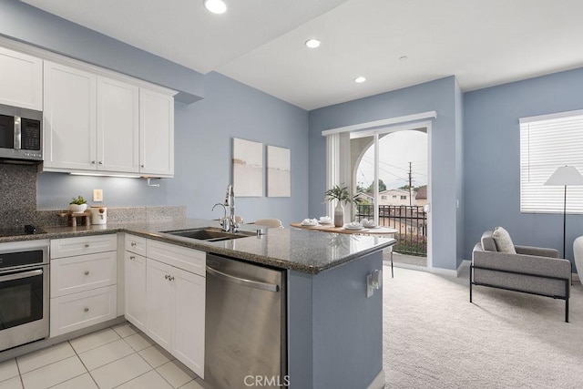 kitchen with stainless steel appliances, a sink, a peninsula, white cabinets, and recessed lighting