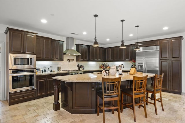 kitchen featuring built in appliances, backsplash, wall chimney exhaust hood, and stone tile floors