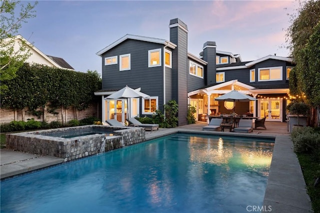 back of property featuring a fenced in pool, a patio, a chimney, an in ground hot tub, and french doors
