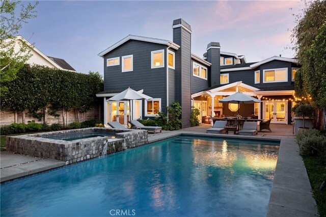 2400 Holly Ln, Newport Beach, CA 92663 - back of property at dusk featuring french doors, an in-ground hot tub, a chimney, an outdoor pool, and a patio area