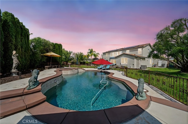 pool at dusk with a patio area, a pool with connected hot tub, and fence