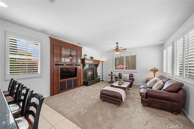 living room featuring light tile patterned floors, baseboards, a ceiling fan, a glass covered fireplace, and light carpet