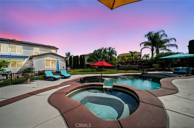 pool at dusk with a patio, a pool with connected hot tub, and fence