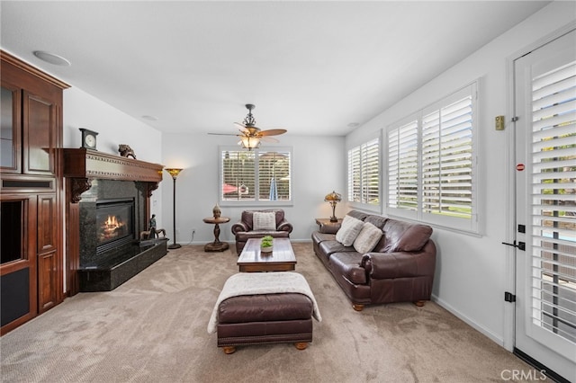 living area featuring a ceiling fan, baseboards, a glass covered fireplace, and carpet