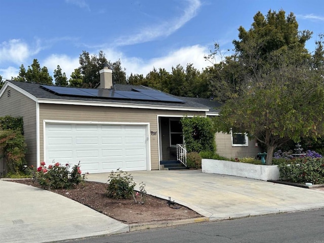view of front of property with driveway, a chimney, an attached garage, and roof mounted solar panels