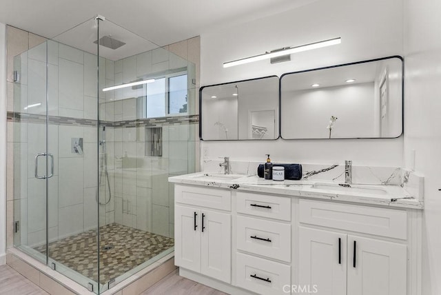 full bathroom with a stall shower, double vanity, and a sink