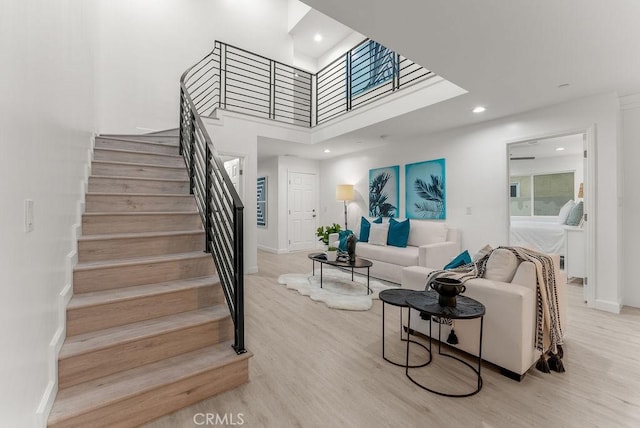 living area featuring baseboards, light wood finished floors, recessed lighting, a towering ceiling, and stairs