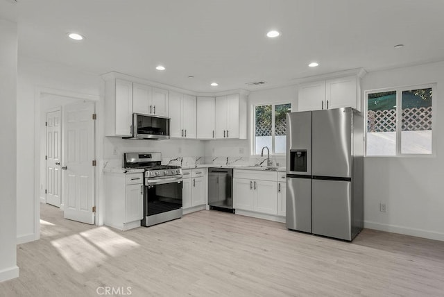 kitchen with baseboards, light wood-type flooring, white cabinets, appliances with stainless steel finishes, and a sink