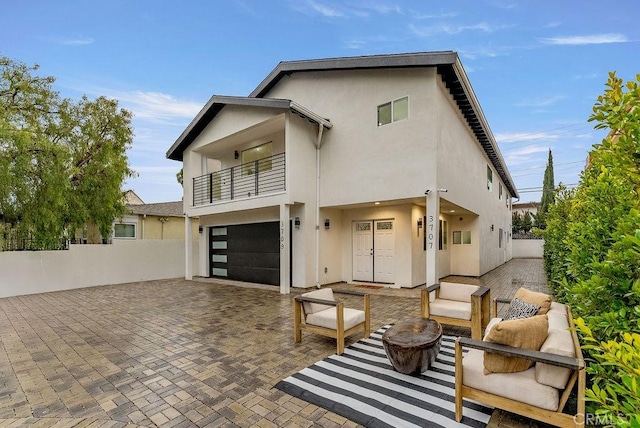 back of property featuring fence, stucco siding, a garage, and a balcony