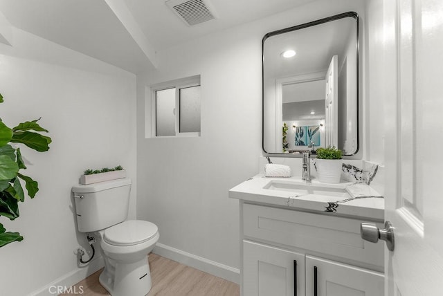bathroom with vanity, visible vents, toilet, wood finished floors, and baseboards