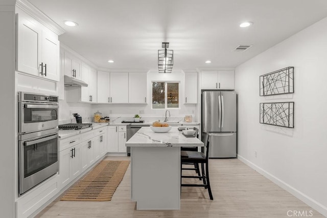 kitchen featuring a kitchen bar, visible vents, under cabinet range hood, stainless steel appliances, and baseboards