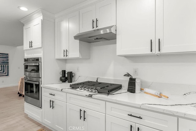 kitchen featuring white cabinets, light wood-type flooring, appliances with stainless steel finishes, under cabinet range hood, and light stone counters