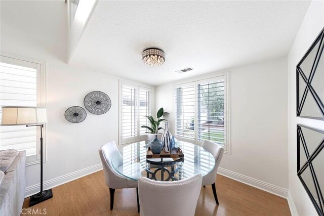 dining area with baseboards, wood finished floors, visible vents, and a textured ceiling