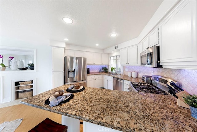 kitchen with white cabinets, stainless steel appliances, a peninsula, a sink, and stone countertops