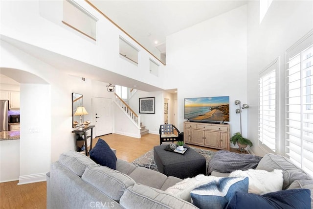 living room featuring light wood-type flooring, a healthy amount of sunlight, and a towering ceiling