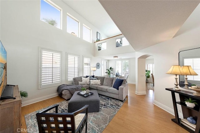 living room with arched walkways, wood finished floors, a towering ceiling, and baseboards