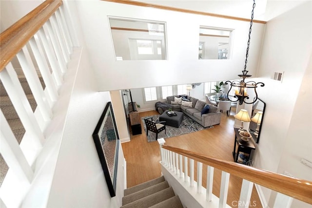 staircase featuring visible vents, a towering ceiling, wood finished floors, and a chandelier