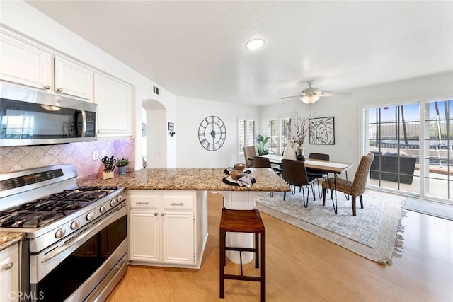 kitchen featuring stainless steel appliances, backsplash, arched walkways, light wood-style flooring, and ceiling fan