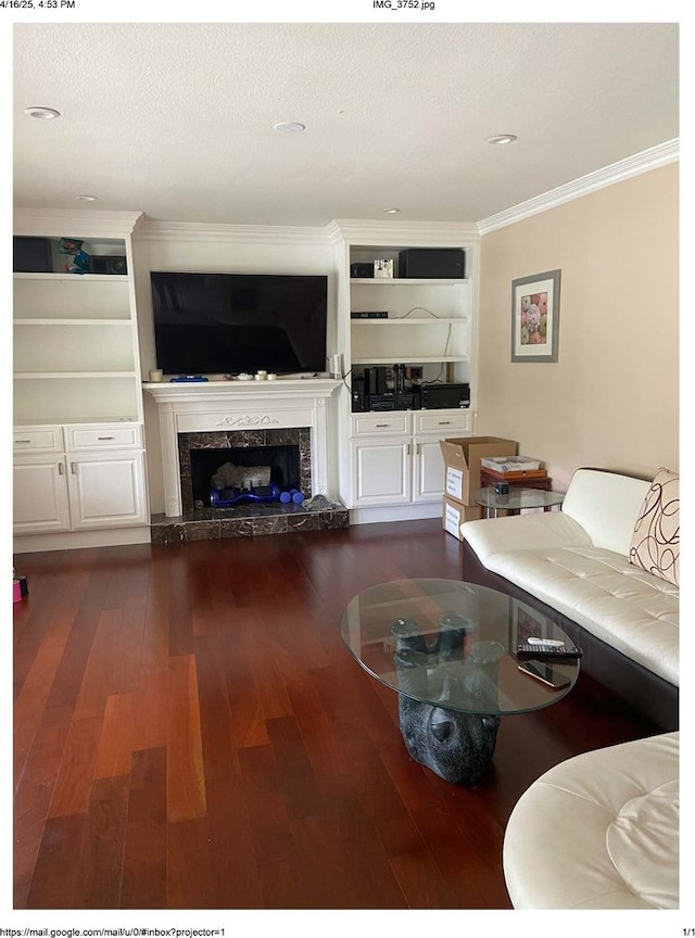 living area with a premium fireplace, ornamental molding, dark wood finished floors, and built in shelves