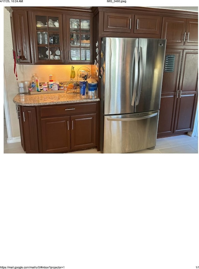 kitchen with light stone countertops, glass insert cabinets, freestanding refrigerator, and dark brown cabinetry