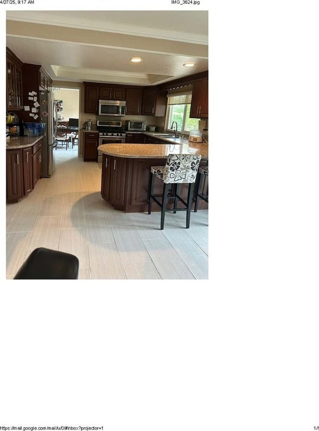 kitchen with a sink, stainless steel appliances, a kitchen breakfast bar, crown molding, and dark brown cabinetry