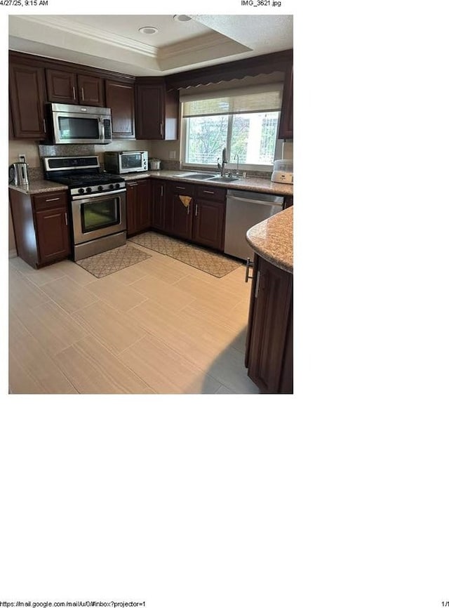 kitchen featuring a sink, stainless steel appliances, a tray ceiling, crown molding, and dark brown cabinetry