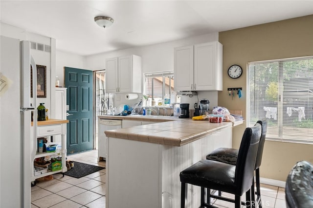 1109 Ivy St, Chico, CA 95928 - kitchen with a peninsula, light tile patterned floors, white cabinetry, a breakfast bar area, and white dishwasher