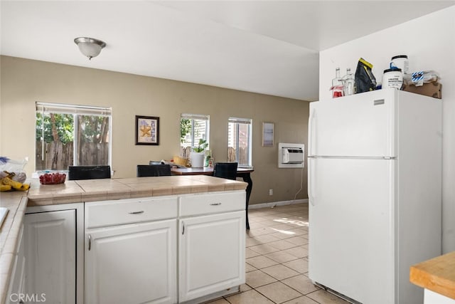 1109 Ivy St, Chico, CA 95928 - kitchen featuring a wall mounted air conditioner, light tile patterned floors, a peninsula, freestanding refrigerator, and white cabinets
