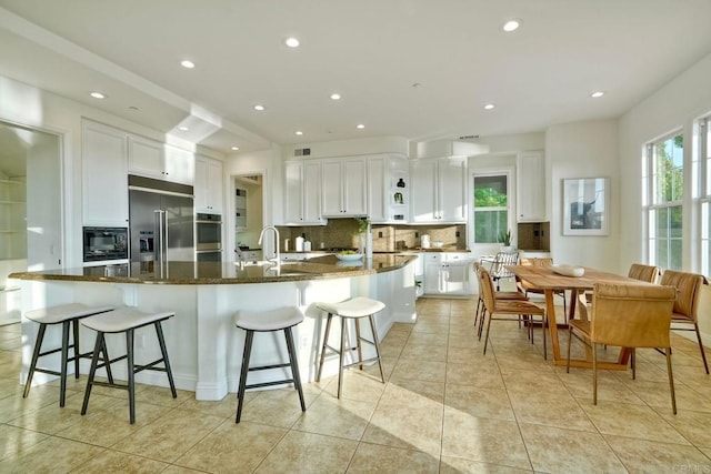 1664 Aryana Dr, Encinitas, CA 92024 - kitchen featuring built in appliances, tasteful backsplash, a large island with sink, white cabinetry, and a kitchen bar