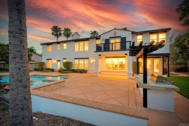 1664 Aryana Dr, Encinitas, CA 92024 - back of house at dusk with a balcony, a patio, an outdoor pool, stucco siding, and an in-ground hot tub