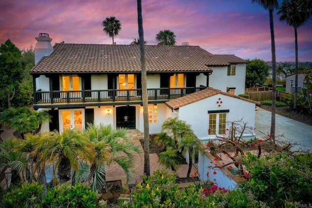 1664 Aryana Dr, Encinitas, CA 92024 - back of house at dusk featuring stucco siding, french doors, a chimney, a tiled roof, and a balcony