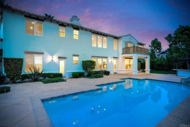1664 Aryana Dr, Encinitas, CA 92024 - back of house at dusk with a balcony, a chimney, a patio, an outdoor pool, and stucco siding