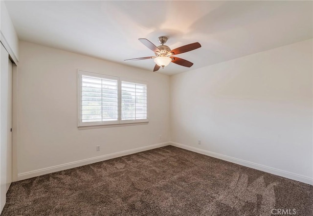 empty room with dark colored carpet, a ceiling fan, and baseboards