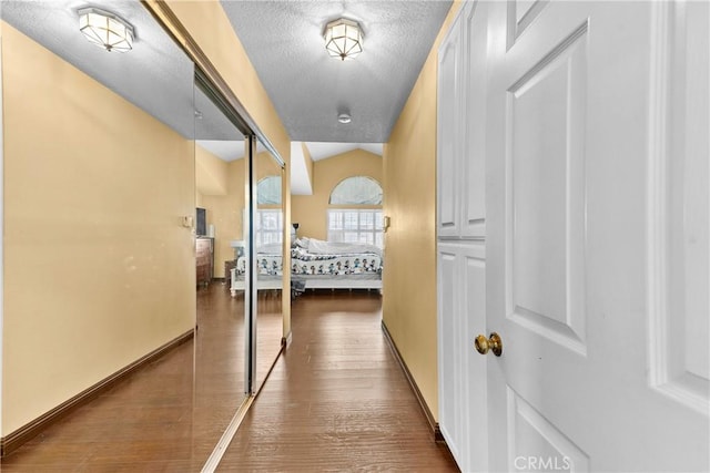 interior space featuring baseboards, vaulted ceiling, a textured ceiling, and wood finished floors