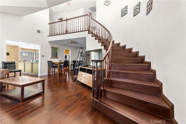 staircase featuring a high ceiling, baseboards, visible vents, and wood finished floors