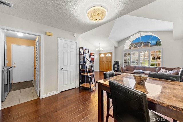 dining space with wood finished floors, separate washer and dryer, a notable chandelier, a textured ceiling, and visible vents