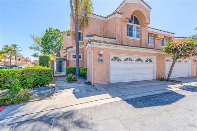 traditional-style home featuring stucco siding, a tiled roof, an attached garage, and a gate