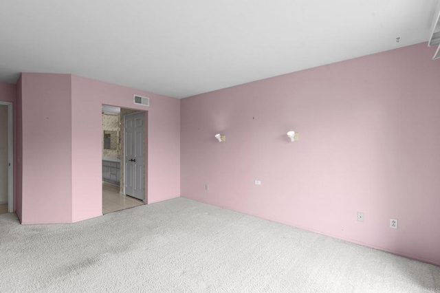 unfurnished bedroom with light colored carpet, ensuite bath, and visible vents