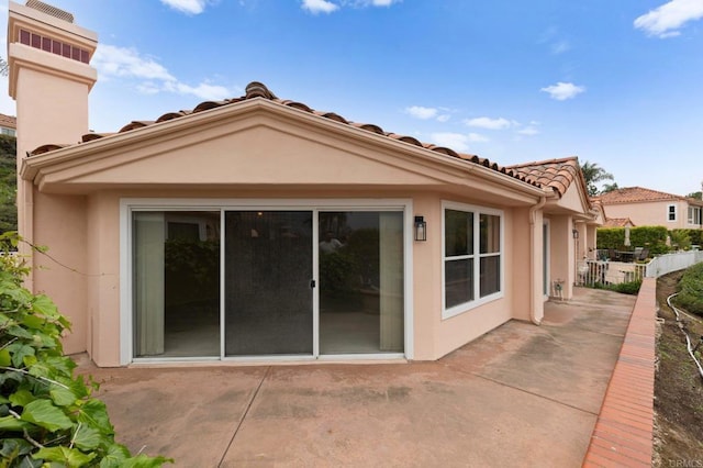 rear view of house with a patio area, a tiled roof, fence, and stucco siding