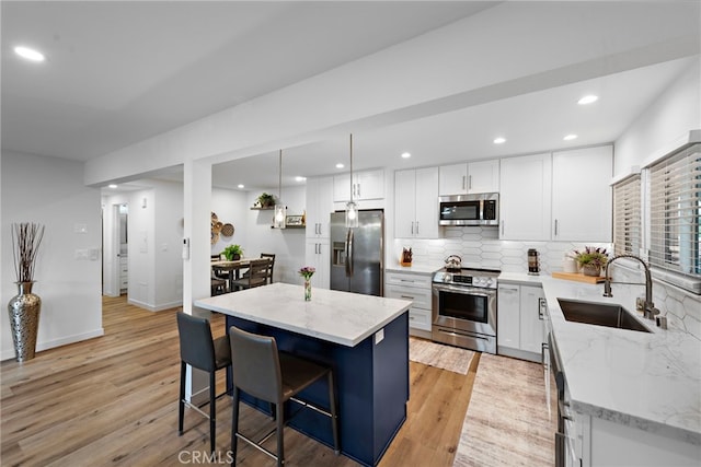 kitchen featuring white cabinets, appliances with stainless steel finishes, a breakfast bar, a sink, and tasteful backsplash