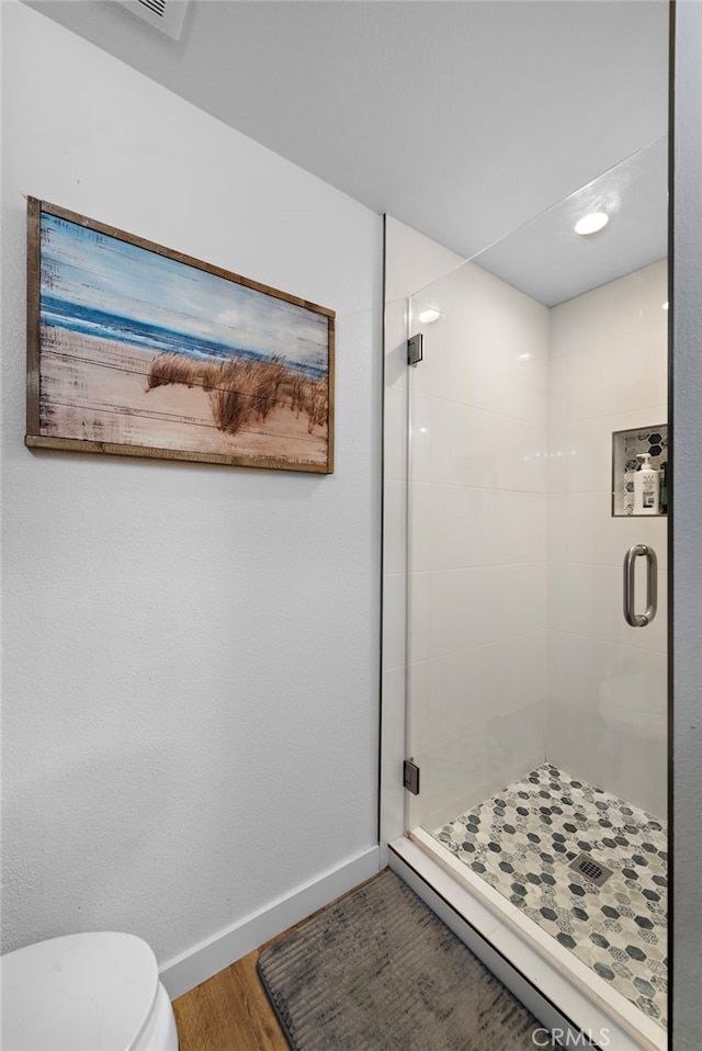 bathroom featuring toilet, baseboards, wood finished floors, and a stall shower