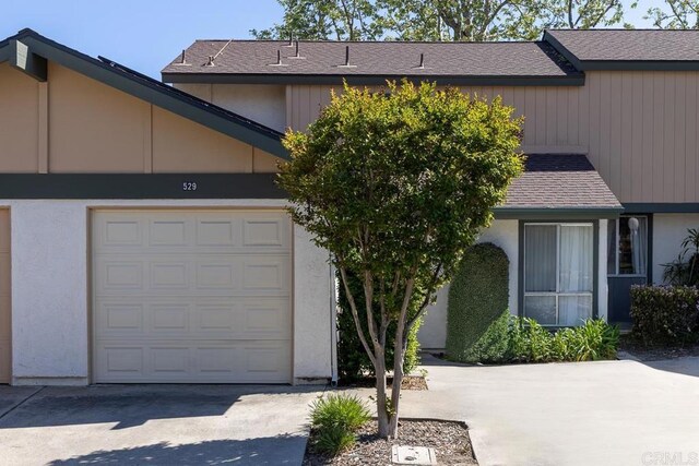 view of front of house with concrete driveway, roof with shingles, and stucco siding