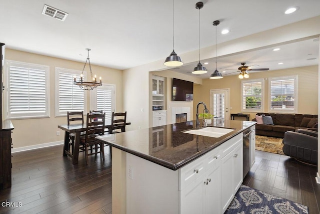 kitchen with a sink, a glass covered fireplace, dark wood finished floors, ceiling fan with notable chandelier, and visible vents