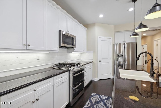 kitchen with white cabinets, a sink, appliances with stainless steel finishes, backsplash, and hanging light fixtures